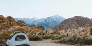 white and black dome tent setted up beside brown boulders overlooking mountain under white sky