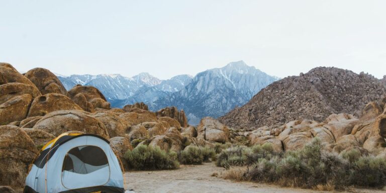 white and black dome tent setted up beside brown boulders overlooking mountain under white sky