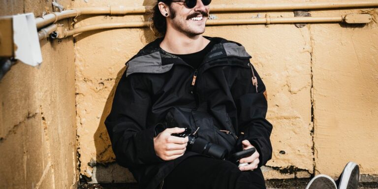 man in black leather jacket and black pants sitting on concrete wall during daytime