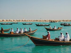 Traditional Emirati boats on turquoise waters with participants celebrating Al Dhafra Water Festival 2024 in traditional attire.