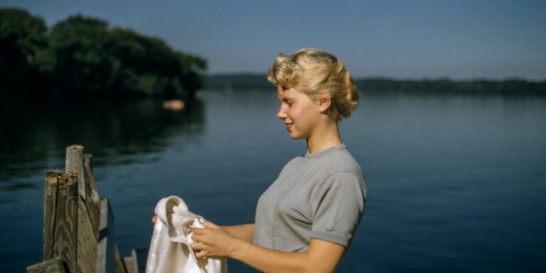 woman holding white textile standing beside body of water