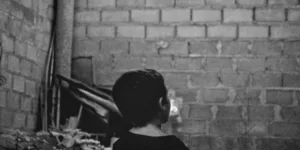 grayscale photo of boy standing near wall