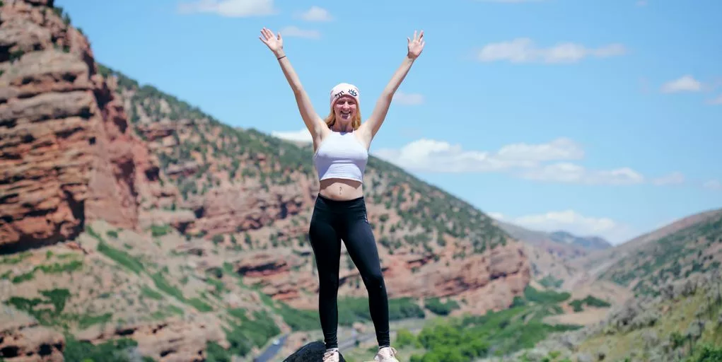 woman wearing white top and black pants standing on cliff