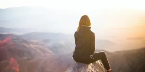 person sitting on top of gray rock overlooking mountain during daytime