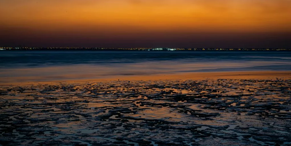 the sun is setting over the water at the beach