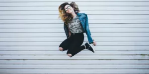 woman jumping in front of white concrete establishment