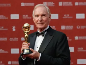 Peter Weir holding award on red carpet.