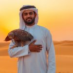 Man in traditional Emirati dress, falcon on arm, desert