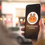 Pancakeswap cryptocurrency symbol, CAKE logo. Business and financial concept. Hand with smartphone, screen with crypto icon close-up