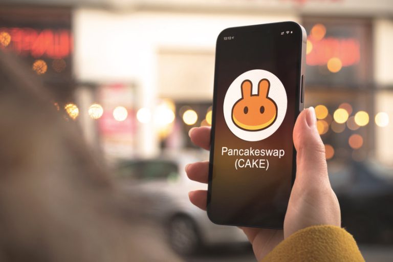 Pancakeswap cryptocurrency symbol, CAKE logo. Business and financial concept. Hand with smartphone, screen with crypto icon close-up