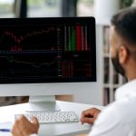 Successful smart concentrated confident Indian broke, trade analyst, sitting at computer in modern office, buying and selling cryptocurrencies, analyzing cryptocurrency market, looking at screen